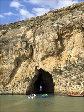 Small fishing boat sails in inland sea of Gozo in tunnel from passage through rock face to open sea