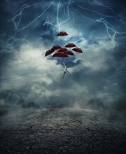 Young man with a lot of umbrellas as an air balloon rise up to the sky full of lightnings