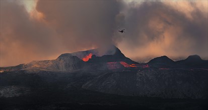 Helicopter flying over erupting volcano with lava fountains and lava field