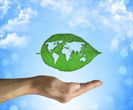 Opened hand holding a green leaf with world map inside on a blue sky background