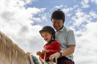 Father and son enjoying horse riding in the paddock