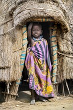 Traditional dressed child of the Jiye tribe standing in her hut