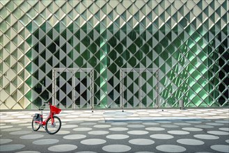 Red rental bike standing in front of the glass facade of the Futurium Museum on Kapelle Ufer