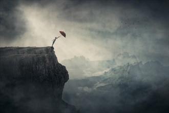Fearless person on the edge of a cliff determined to catch his umbrella and fly away over abyss