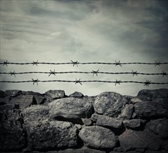 Masonry stone wall fence of a prison with barbed metallic wire above