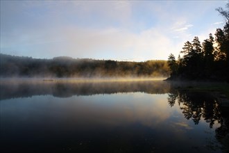 Morning fog drifts over a lake at sunrise