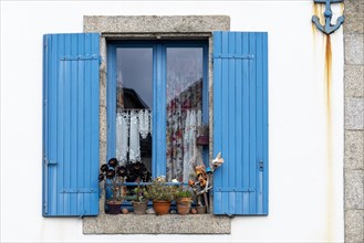 Closed window with blue wooden shutters with flowers in front and maritime anchor on the facade in Ville Close