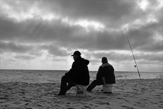 Two anglers sitting on buckets on the beach