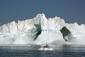 Small fishing boat in front of huge iceberg with two large caves