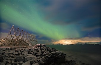 Aurora borealis over a worker in a wooden stockfish rack