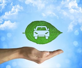 Opened hand holding a green leaf with a car icon inside on a blue sky background