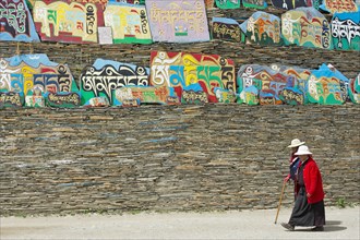 Two Tibetan women walking around a huge piled stack of mani stones with Tibetan writing at a Tibetan monastery in the grasslands of Tagong