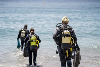 Three scuba divers with all equipment heading to the sea