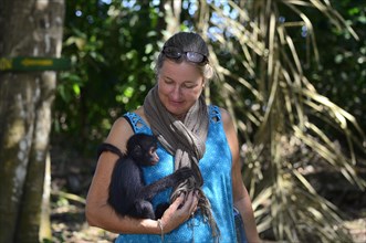 Tourist cuddles with a young peruvian spider monkeys