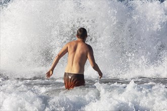 Young man jumps into a high wave on the beach of Praia de Santa Barbara