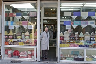 Man in a smock standing in front of his shop with sweets