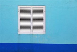 Light blue house facade with closed white shutters