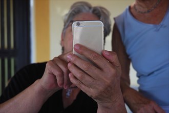 Two older woman help each other with mobile phone operation