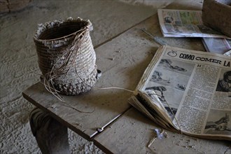 Frayed basket of esparto grass on dusty wooden table with newspapers