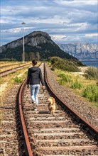 Young woman with dog walking on the disused railway bed in the town of Figari