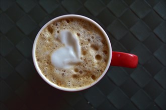 Heart symbol in the foam of a red coffee cup