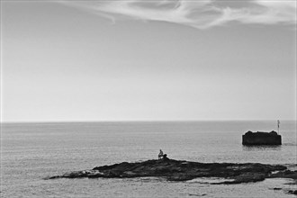 Man sitting alone on small rocky island