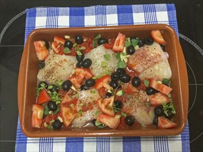 Cod fish in a clay dish with olives