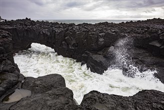 Lava arch on the volcanic coast at high tide with high waves