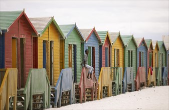 Man sitting on fence in front of colourful beach huts
