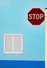 Light blue house facade with closed white shutters and stop sign