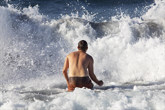 Young man jumps into a high wave on the beach of Praia de Santa Barbara