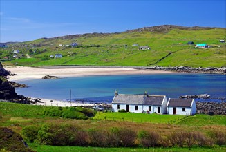 Small cottage in front of long sandy beach in green landscape