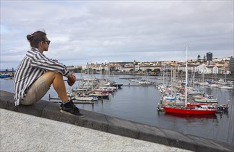 Young man sitting on the promenade in the marina of Ponta Delgada