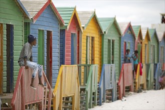 Man sitting on fence in front of colourful beach huts