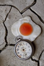 Handless pocket watch with fried egg on dried clay floor