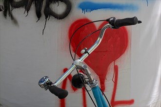 Handlebars from bicycle in front of wall with red heart symbol