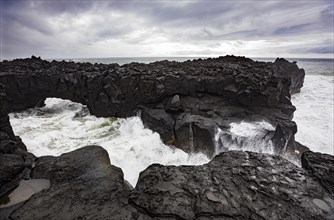Lava arch on the volcanic coast at high tide with high waves