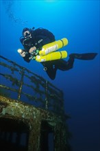 Diver swims over shipwreck has special equipment carries stage tanks for mixed gas diving