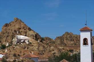 Mountain with cave house and white church tower in cave district of Guadix