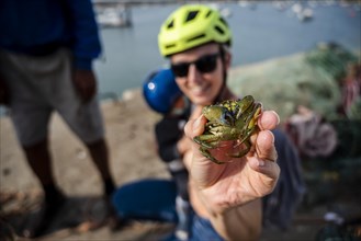 A tourist woman enjoys holding a green crab in her hand in the harbor of Alvor