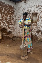 Woman grinding cassava with a post and wooden pot to create Cassava flour to be used in baking. Rwanda