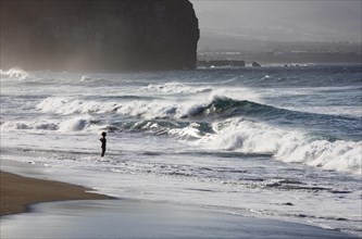 A woman standing on the sandy beach of Praia de Santa Barbara in stormy sea with high waves