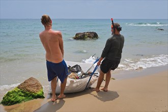 Two young men on the beach pulling heavy bag of plastic waste