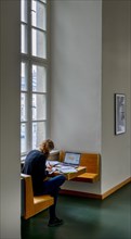 A student sits studying with her laptop at the window in the building of the Humboldt University