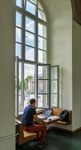 A student sits studying with his laptop at the window in the building of the Humboldt University