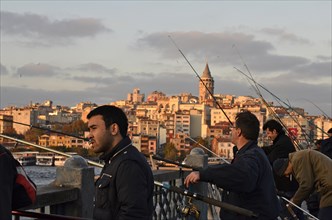 Anglers at the Golden Horn on Galata Bridge with view the Galata Tower at sunset