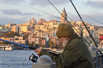 Old man with cap fishing at the Golden Horn on Galata Bridge with view the Galata Tower at sunset