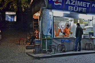 Kebab shop illuminated at night with vendor and customers