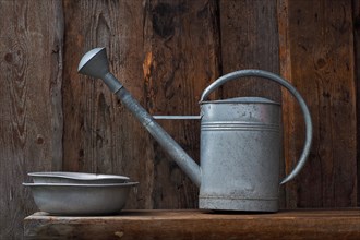 Zinc watering can and zinc bowls on wooden bench in front of wooden wall