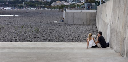 Young couple sitting on a concrete staircase on a pebble beach in Funchal